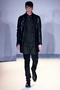 Мужское прямое кожаное пальто чёрного цвета от Edun в сочетании с рубашкой чёрного тона Edun, брюками чёрной расцветки Edun и чёрными туфлями Edun.
