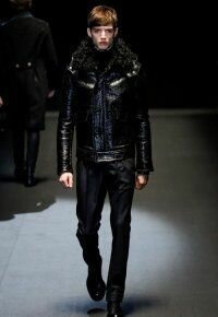 Короткое кожаное пальто двубортного фасона с меховым воротником из коллекции Gucci в сочетании с классическими чёрными брюками Gucci и туфлями чёрного тона Gucci.