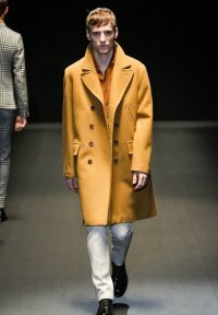 Кожаное зимнее пальто солнечно-жёлтого оттенка двубортного фасона с длиной выше колен от Gucci в сочетании с рубашкой оранжевого тона, белыми брюками Gucci и туфлями чёрного цвета от Gucci.