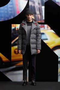 Стеганое пуховое пальто серого цвета средней длины с капюшоном от DKNY в сочетании с брюками чёрного тона, серым свитером DKNY и чёрными туфлями DKNY.
