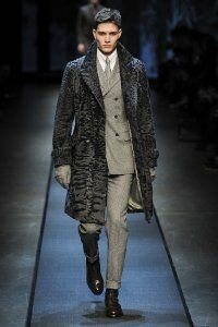 Зимнее мужское пальто средней длины серой расцветки с меховой отделкой из коллекции Canali в сочетании с брючным костюмом светло-серого оттенка Canali и туфлями шоколадного тона Canali.