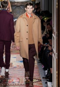 Зимнее мужское пальто однобортного фасона цвета капучино из коллекции Valentino в сочетании с вязаным свитером светло-коричневого оттенка, брюками сливового тона Valentino и кроссовками серо-коричневой расцветки от Valentino.