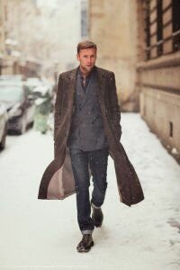 Длинное мужское пальто серо-коричневого оттенка в сочетании с брючным костюмом серого цвета и туфлями чёрно-коричневого тона.