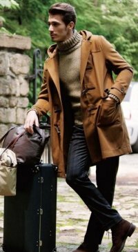 Мужское зимнее пальто дафлкот коричневого цвета средней длины с капюшоном в сочетании с вязаным свитером серо-коричневого оттенка, брюками в клетку синего тона и ботинками тёмно-коричневой расцветки.