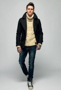 Короткое мужское пальто чёрного цвета приталенного силуэта в сочетании с вязаным свитером молочного оттенка, синими джинсами и кроссовками чёрно-белого тона.