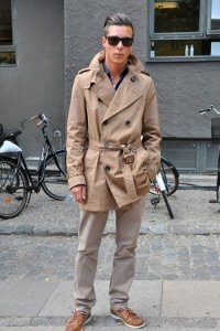 Мужское пальто светло-коричневого оттенка средней длины двубортного фасона с тонким поясом в сочетании с брюками светло-серого тона и туфлями коричневого цвета.