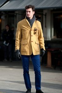 Короткое мужское пальто жёлтого цвета однобортного фасона с накладными карманами в сочетании с джинсами синего тона, шарфом угольного оттенка и туфлями чёрной расцветки.