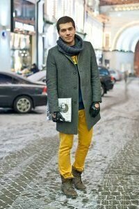 Мужское пальто на зиму грифельного оттенка однобортного фасона в сочетании в шарфом серого цвета, свитером синего тона, брюками солнечно-жёлтой расцветки и ботиками серо-коричневого оттенка.